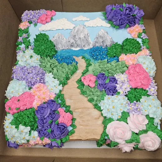 A sheet cake piped as a garden path through buttercream flowers toward snowy mountains