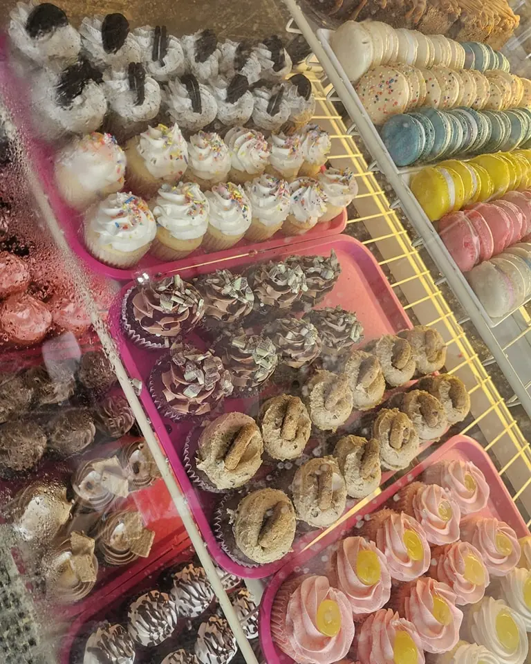A bakery case packed with trays of frosted cupcakes and rows of pastel macarons