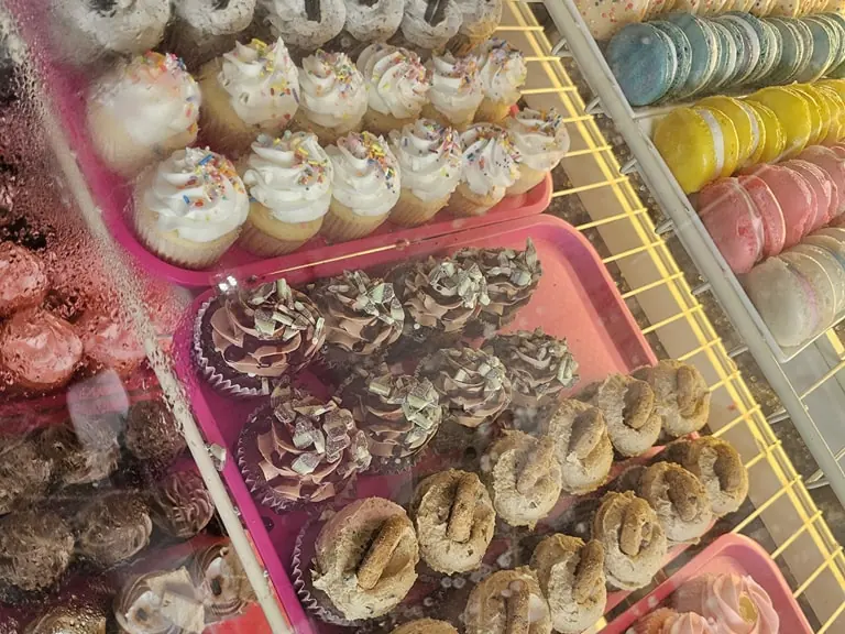 A bakery case packed with trays of frosted cupcakes and rows of pastel macarons