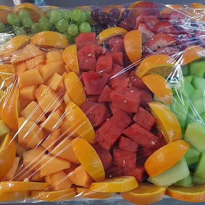 A wrapped tray of melon, pineapple, and grapes