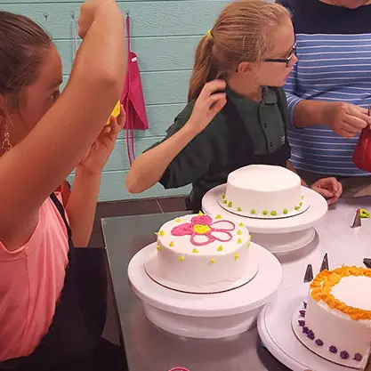 A girl decorating a white cake with pink flowers