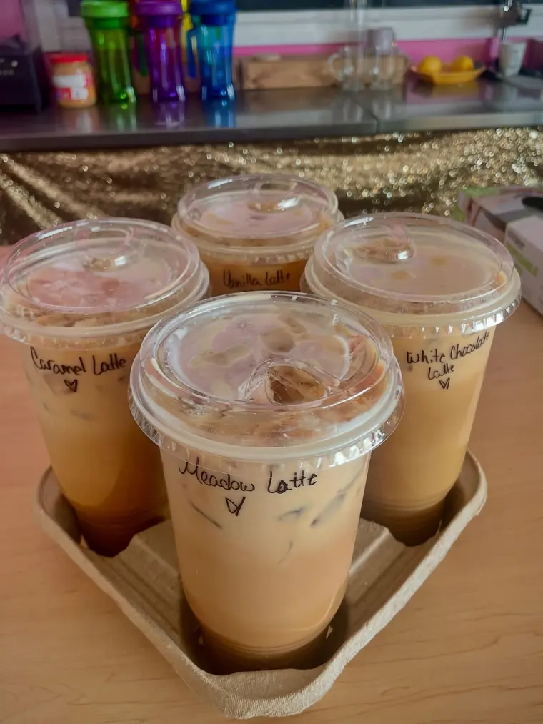 Four iced lattes in a drink carrier, each with its flavor handwritten on the lid