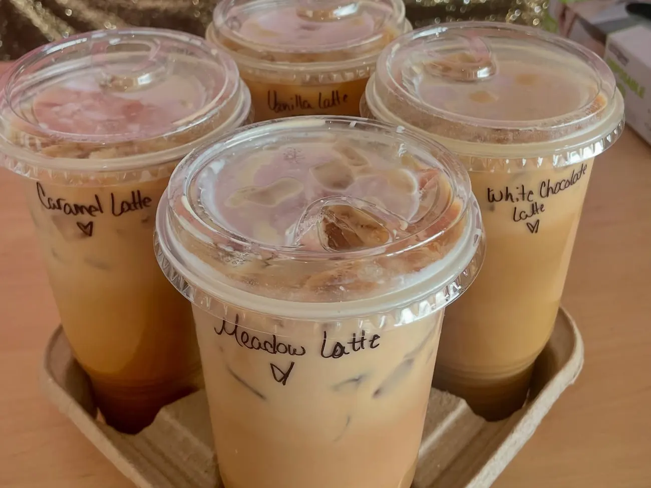 Four iced lattes in a drink carrier, each with its flavor handwritten on the lid