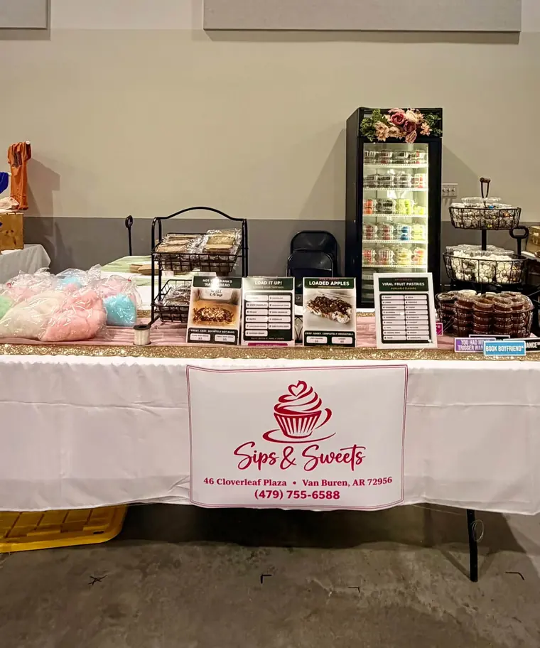 The Sips & Sweets pop-up table at an event, set with cotton candy, boxed treats, and menus